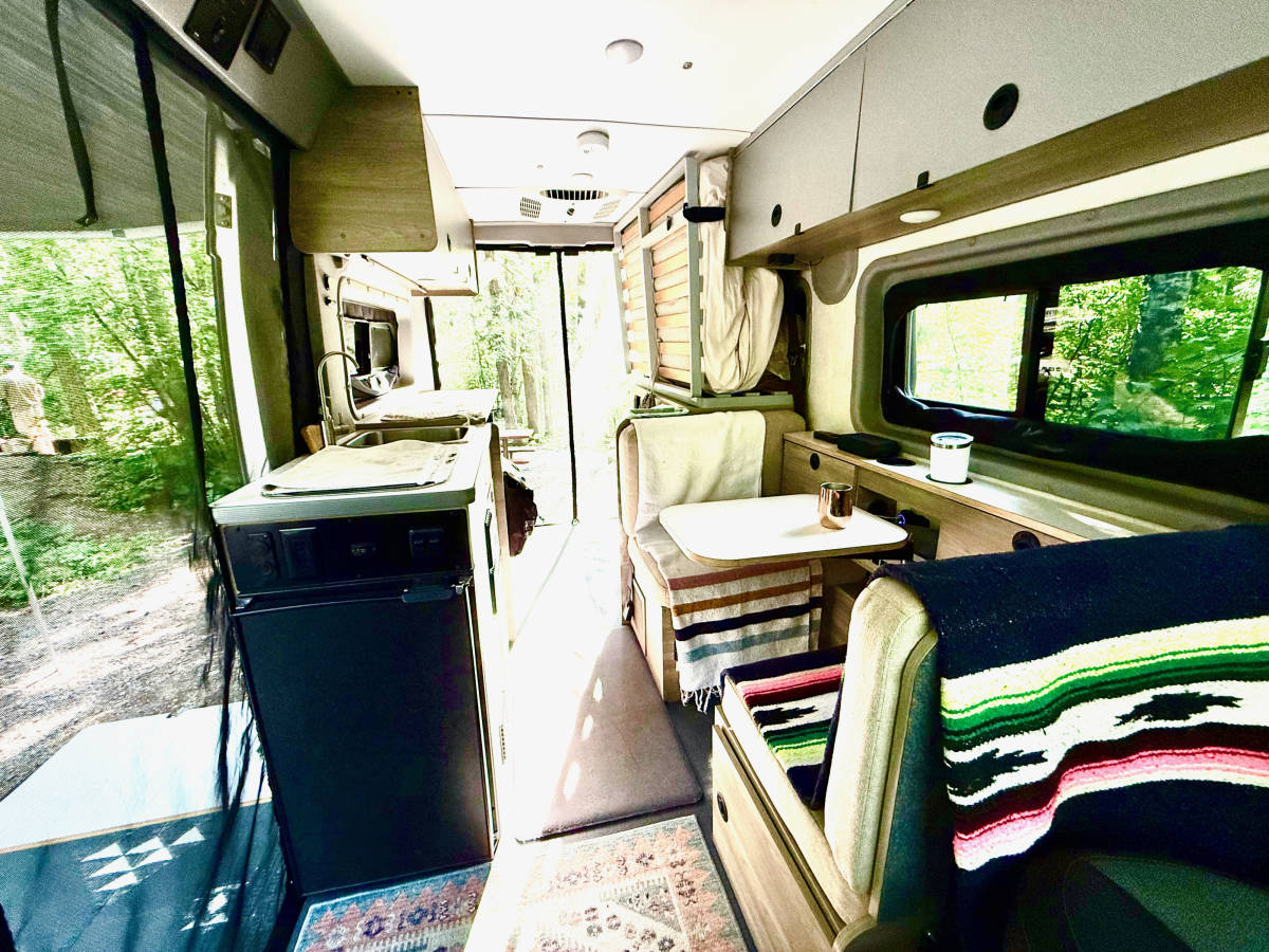 The interior facing the rear: fridge on the left, dinette on the right, the ceiling unit overhead and the bed folded up at the back.