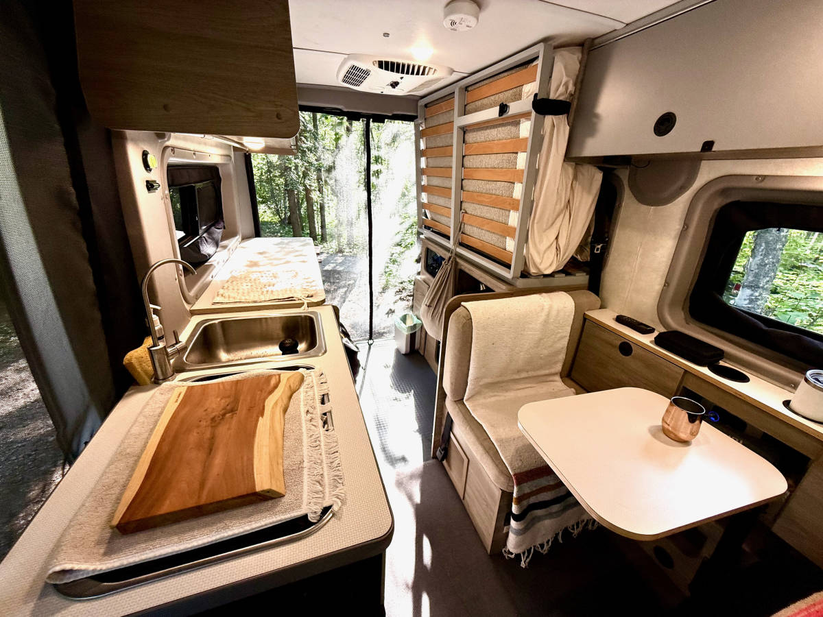The galley counter with a stainless sink and a wooden cutting board, the dinette across the aisle and the bed folded up against the wall.