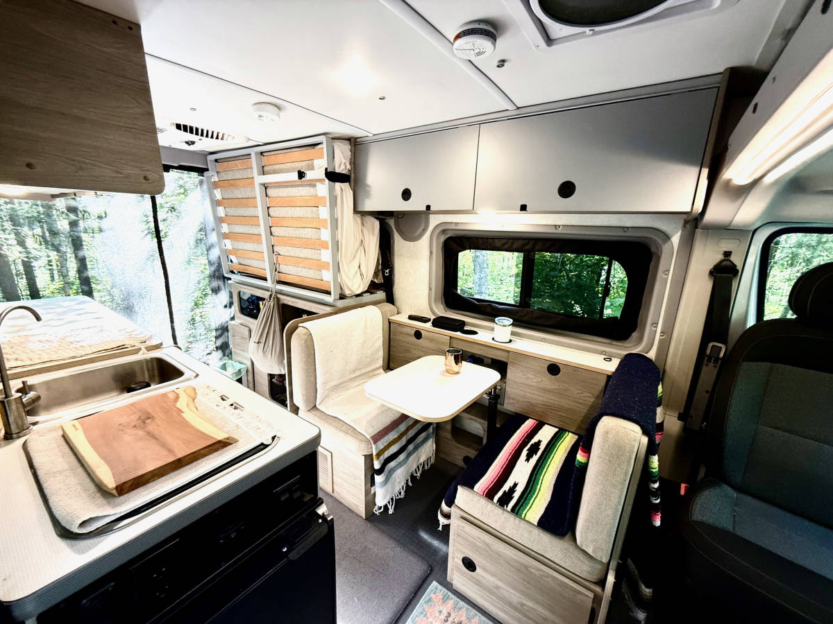The dinette: two facing seats and a small table under the side window, with overhead cabinets above.