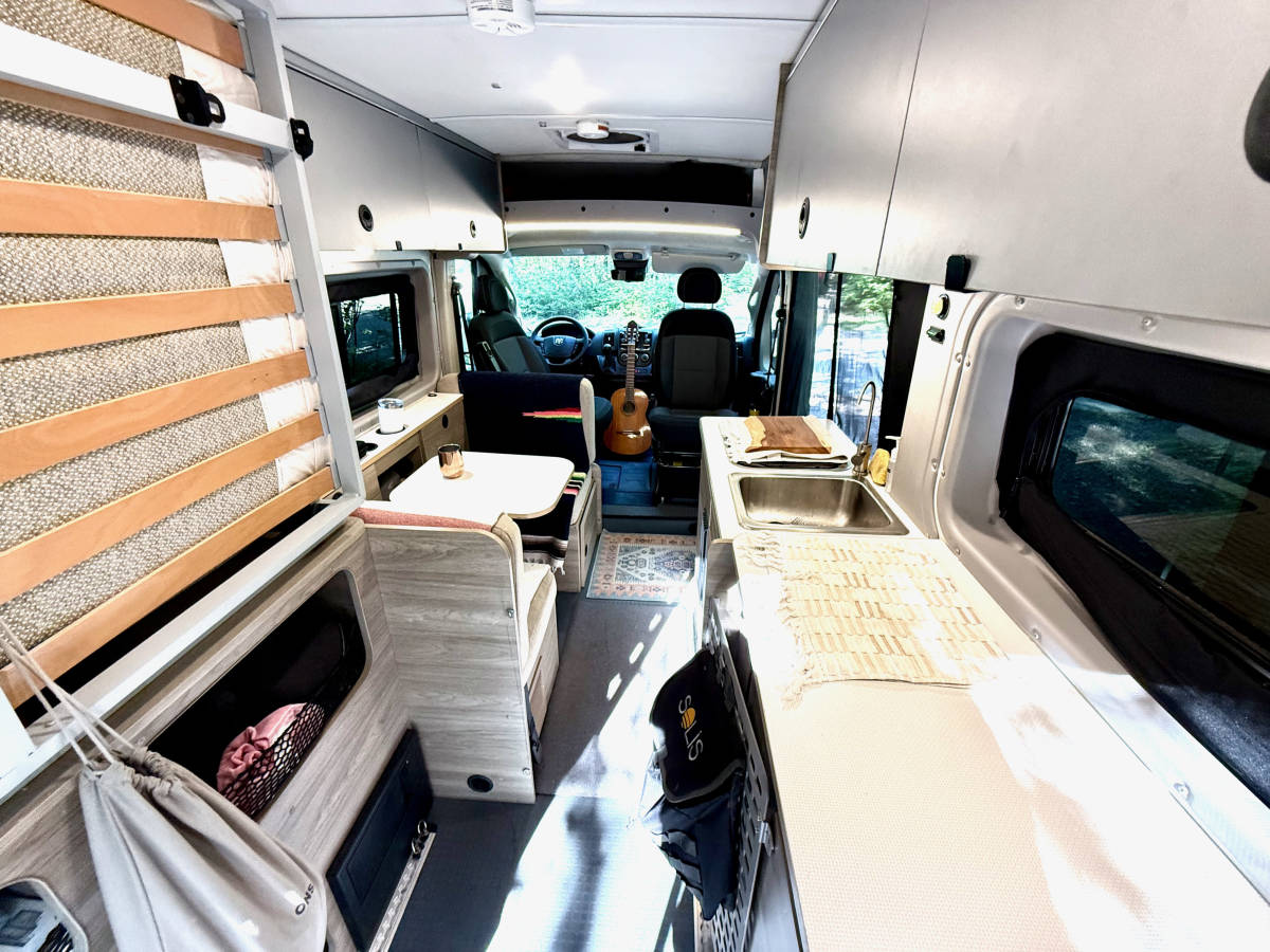 The full length of the van looking forward from the back: the bed folded up on the left, the galley on the right and a guitar resting on the cab seat.